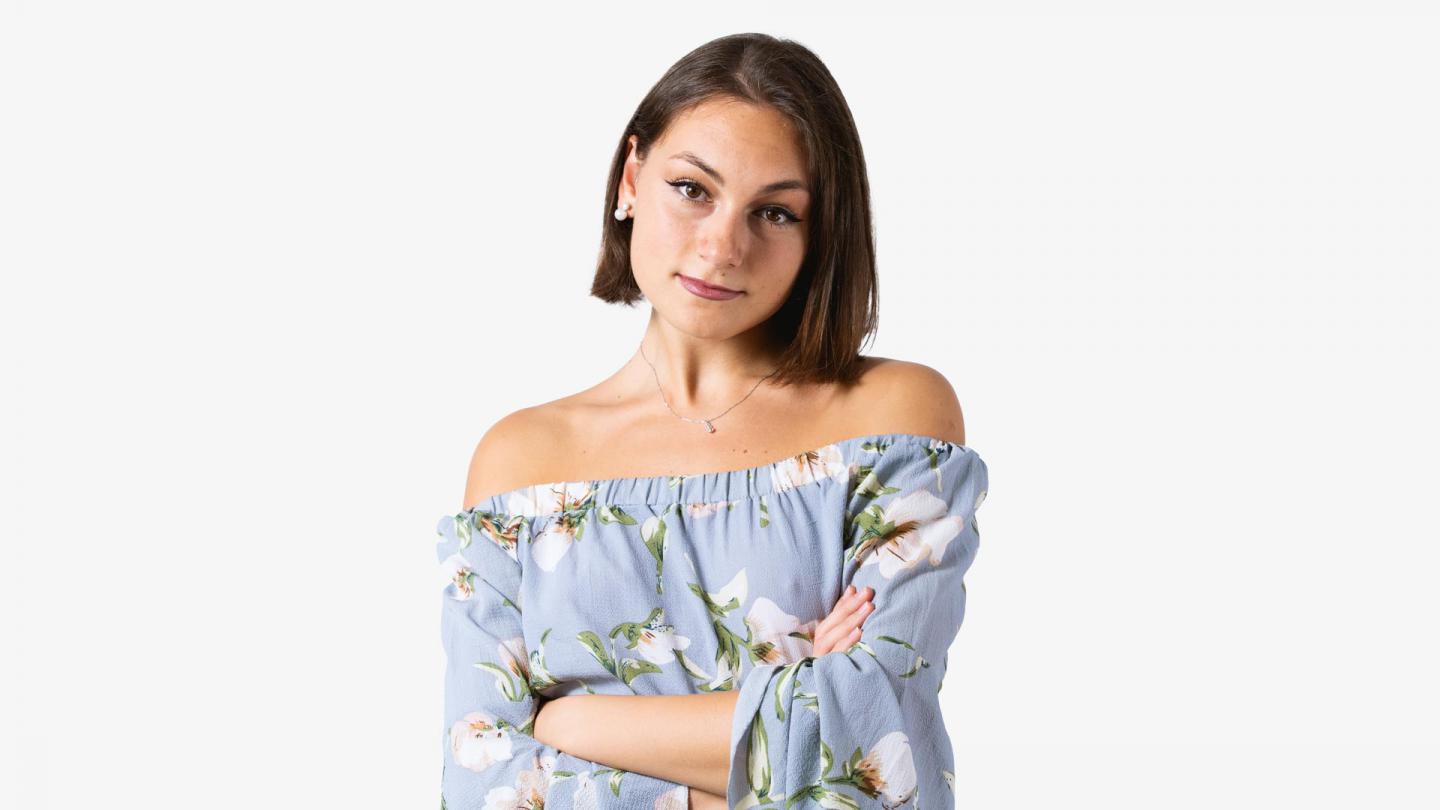 A headshot of a woman looking forward with dark brown hair and a light blue flowery top