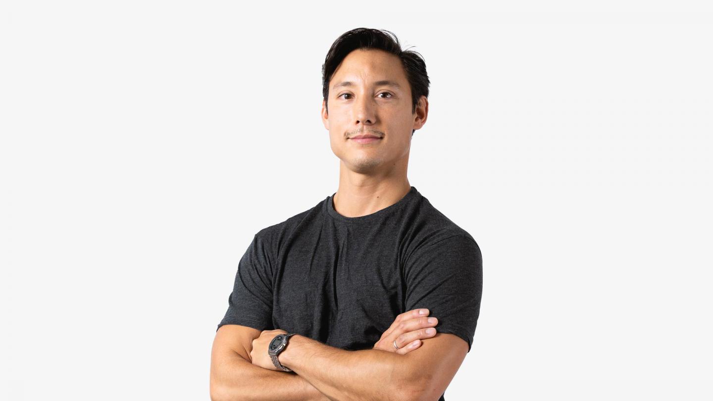 A headshot of a man stood with arms crossed in a dark grey t-shirt