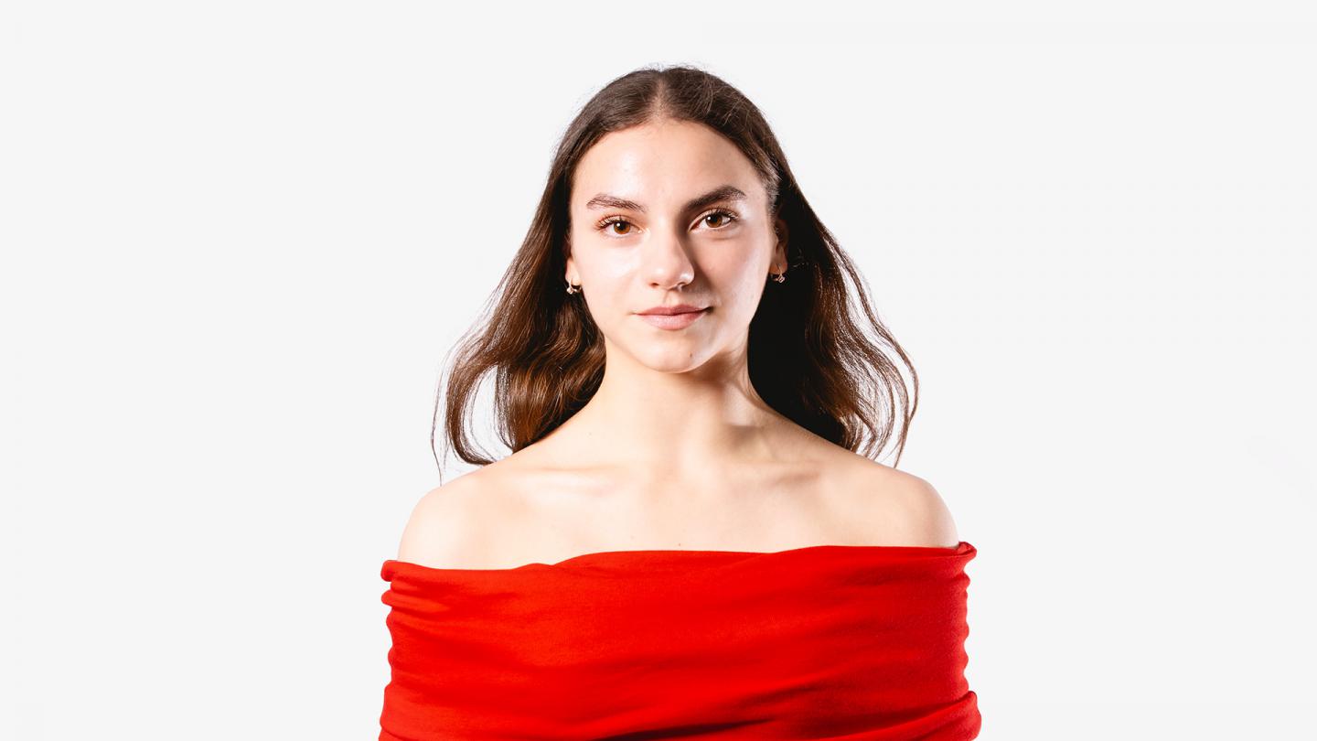 Woman with long, straight, dark hair, wearing a vivid red dress, looks directly at the camera