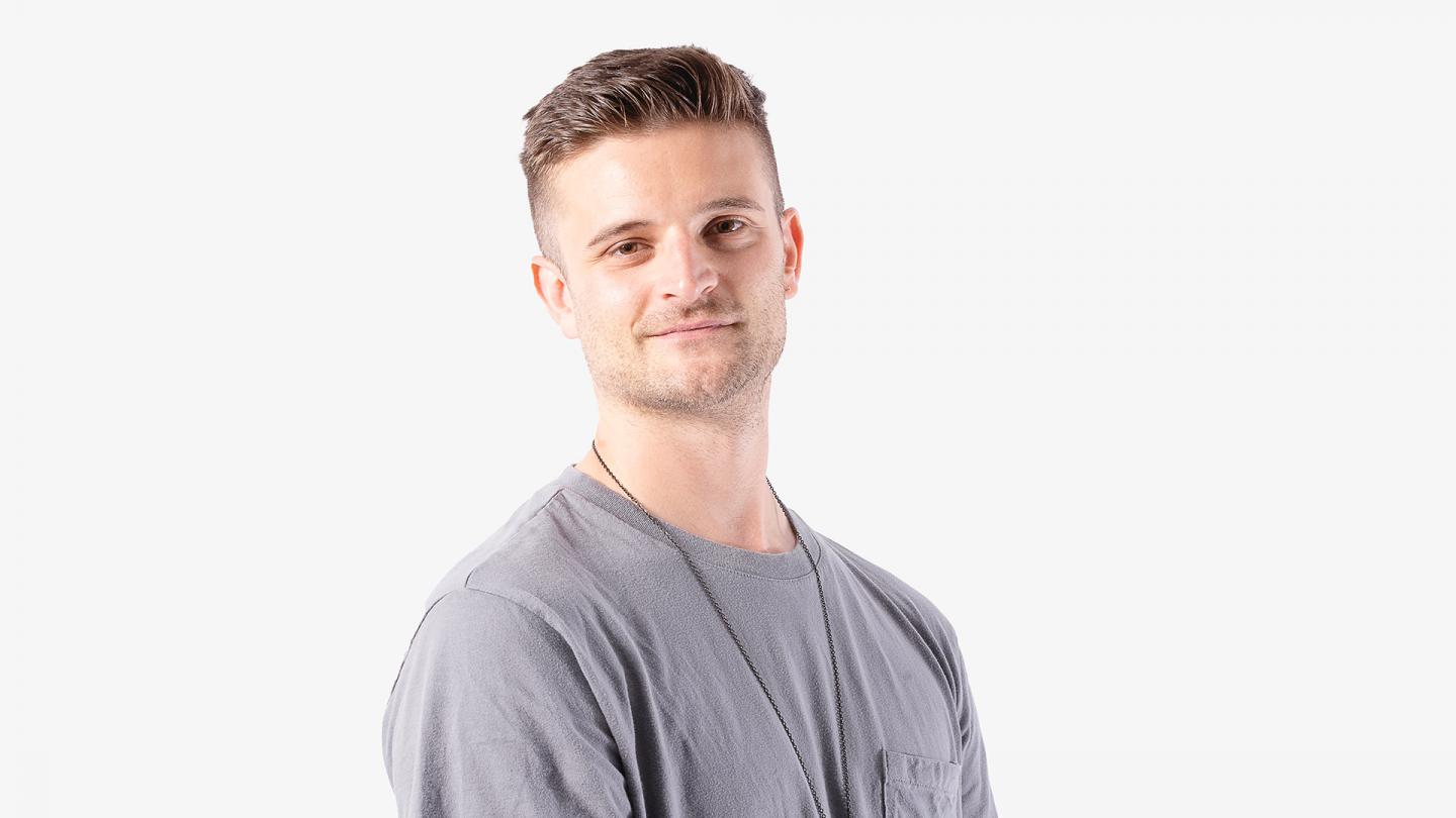 Man wearing a grey T-shirt, short brown hair, smiling wanly at the camera