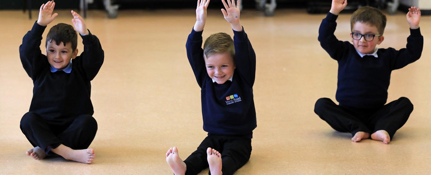 Three boys sat on the floor with hands above their heads