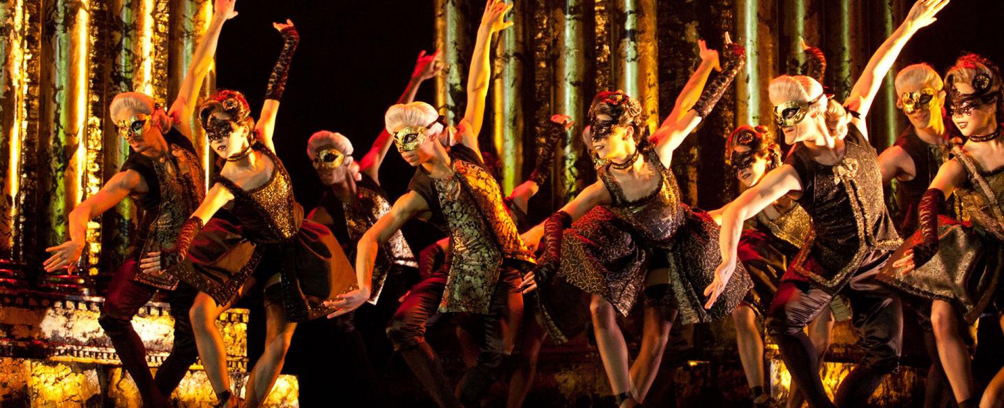 A groups of dancers on stage in masks and 18th century attire