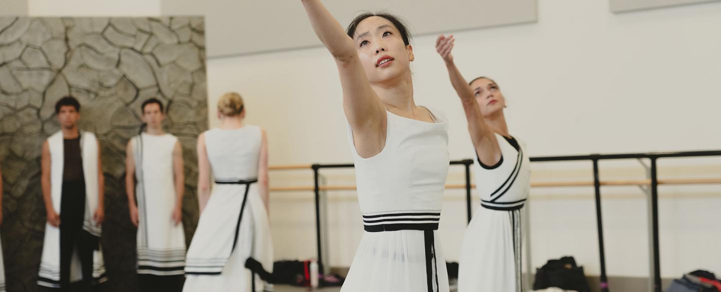 Dancers stands one arm raised and following that line with their gaze.