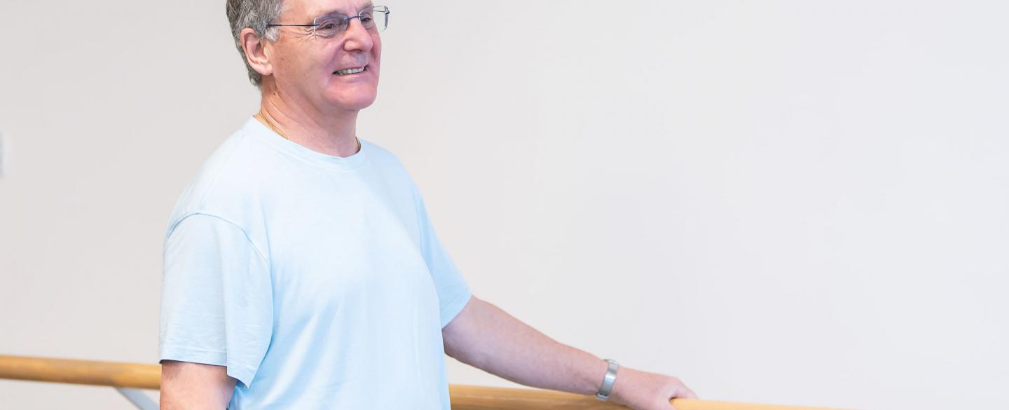 A man stood smiling, holding onto the ballet barre