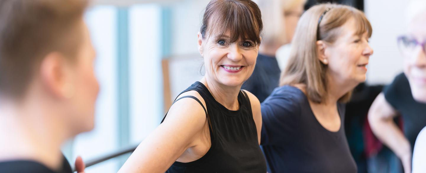 A woman stood relaxing by a ballet barre smiling