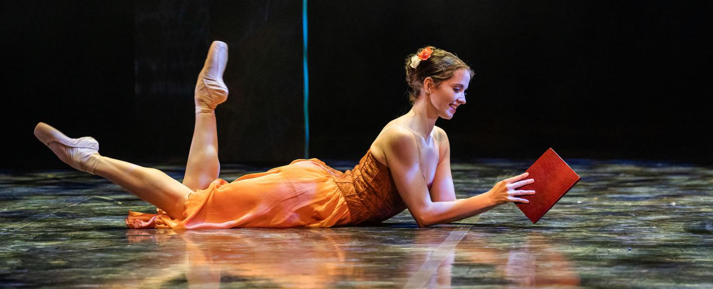 Dancer in an orange dress holding a book 