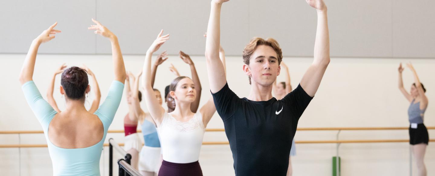 Students in a dance studio practice their poses at a bar