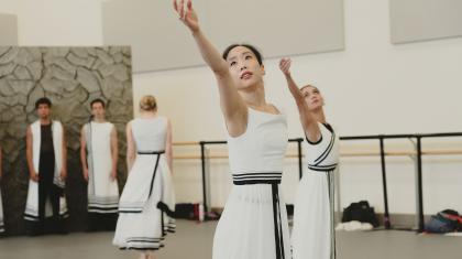 Dancers stands one arm raised and following that line with their gaze.