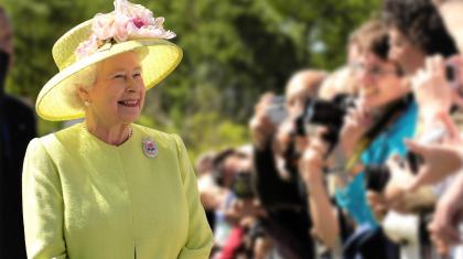 Queen Elizabeth II in a yellow/green outfit standing in front of photographers