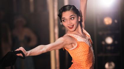 Female dancer on stage in an orange dress, photographed from the 