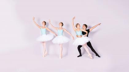 Three female dancers in white tutus stood on pointe. A male dancer holds one dancer sideways