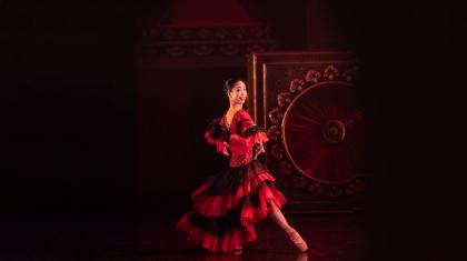 Woman with dark hair tied up dancing in a flowing black and red dress