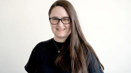 Woman with long hair, glasses and a black T-shirt smiling at the camera