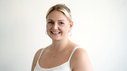 Woman with blonde hair tied back wearing a white vest smiles straight at the camera