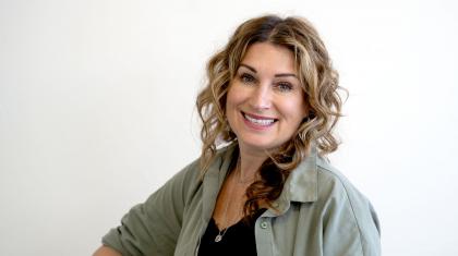 Woman with curly blonde hair wearing a black top under a green shirt, smiles at the camera