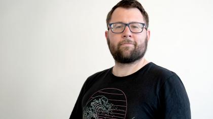 Man with dark hair and beard wearing a dark T-shirt with stylised Hokusai waves looking straight at the camera