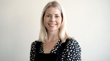 Blonde woman wearing a dark shirt with a white pattern smiles at the camera