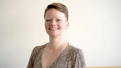 Woman with short fair hair, wearing a patterned top, smiles at the camera