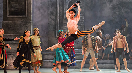 Dancer joyously leaps high above the stage while others look on in wonderment