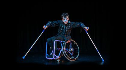 Man in a wheelchair against a black stage looking intently at the camera