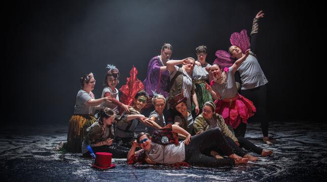 Dancers posing for a poster image dressed in their costumes of grey T-shirts jazzed-up with feather boas, wings, colourful waistcoats, hats and more